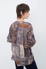 Camisa de corte recto con cuello mao y cierre frontal parcial de botones. Presenta un diseño estampado tipo patchwork con motivos florales y geométricos en tonos tierra, marrones y beige. Posee mangas tres cuartos con puños simples.