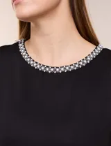 Blusa de silueta recta confeccionada en crepe elastizado, color negro, con escote a la base destacado con una delicada tira aplicada de perlas y cuentas, mangas cortas dollman y ruedo recto.