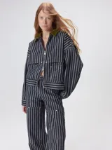 Campera de denim a rayas verticales con cuello de pana en color bordó. Presenta cierre frontal, mangas desmontables con cierre en los hombros, canesú en el pecho y bolsillos de parche cuadrados.