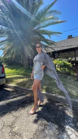 Vestido corto de dos piezas compuesto por una base strapless con frunces y acabado satinado, acompañada de una capa transparente desmontable de corte asimétrico.