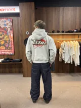 Buzo con capucha gris jaspeado, de corte holgado, con estampado gráfico en la espalda que incluye el texto 'Ittai Company' y una figura de un animal en color rojo.