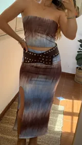 Conjunto de dos piezas compuesto por un top strapless y una falda midi con tajo lateral. Presenta un estampado tipo tie-dye en tonos marrones y celestes. Confeccionado en tejido elástico.
