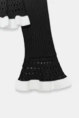 Jersey de punto acanalado en color negro con detalles en blanco. Presenta escote redondo, mangas largas con puños acampanados y detalle de volante en el bajo.
