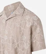 Camisa de poliéster color beige con bordado floral blanco, de corte regular, cuello inglés, manga corta y abotonada en el frente.