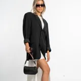 Cartera tipo baguette de color negro, confeccionada en eco cuero con textura granulada. Presenta un diseño compacto con cierre superior y una correa ajustable con detalles en tonos rojizos.