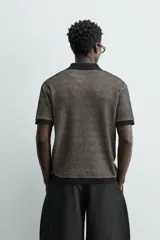 Polo de manga corta con cuello solapa y cierre frontal de dos botones. Tejido de punto con textura de rombos en tonos negro y beige, con ribetes negros en cuello, mangas y bajo.