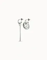 Par de aros asimétricos plateados. Uno es un aro con dije colgante en forma de aguja de coser. El otro es un aro con dije colgante en forma de botón con cuatro agujeros.