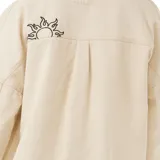 Campera color beige de corte recto, con cuello camisero, cierre frontal con botones a presión y bolsillos con solapa en el pecho. Presenta bordados decorativos en el frente y la espalda.