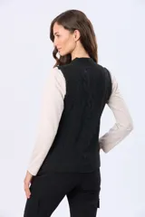 Chaleco tejido de punto grueso en color beige, con cuello redondo y diseño estructurado con detalles de trenzas verticales. Presenta un pequeño aplique de cuero sintético en la parte inferior.