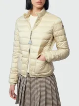 Campera corta acolchada Moncler modelo Lans, color beige, con cuello alto, cierre frontal con tirador personalizado, bolsillos laterales y logo de la marca en la manga izquierda.