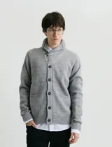 Cardigan de punto color marrón con cuello esmoquin, cierre frontal con botones y presilla superior. Presenta mangas largas con coderas en contraste y bolsillos frontales de ribete.