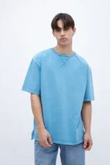 Remera oversize de algodón color celeste, teñida en prenda con efecto lavado. Tiene cuello redondo con detalle de costura en V, mangas cortas, tajos laterales y el largo trasero es más largo que el delantero.