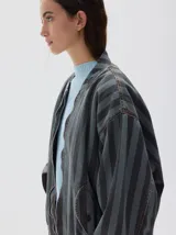 Campera bomber de denim con estampado de rayas verticales en tonos grises, cierre metálico frontal y bolsillos. Presenta un corte oversized y puños y cintura elásticos.