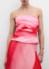 Top palabra de honor con diseño drapeado y entallado. Presenta un estampado degradado en tonos rosados y rojos, con cierre de cremallera invisible en el lateral.