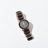 Reloj de pulsera analógico para mujer con caja redonda en tono oro rosado y esfera negra. La correa combina eslabones metálicos en oro rosado con inserciones de cerámica o resina negra.