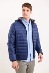 Campera capitoneada color azul marino, con capucha de algodón gris desmontable y cierre frontal. Tiene dos bolsillos exteriores con cierre.