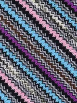 Chal tipo bufanda de lana, con diseño de zigzag vertical en múltiples colores vibrantes como marrón, negro, rojo, naranja y violeta. Presenta flecos en los bordes.