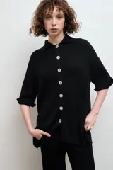 Camisa negra de tejido de punto acanalado, con cuello tipo polo y botones blancos.