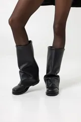 Botas de caña alta confeccionadas en ecocuero negro, con diseño holgado y suela plana con plataforma baja.