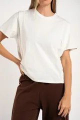 Remera de algodón color mostaza/naranja quemado, con cuello redondo y mangas cortas. Presenta un diseño con costuras externas visibles en los hombros y laterales, dándole un aspecto desestructurado.