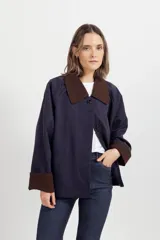 Chaqueta corta de color beige con cuello y puños vueltos en contraste de color azul marino, cierre frontal de botones oscuros y bolsillos ribeteados.