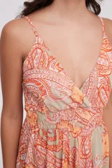 Vestido largo de tirantes finos con escote en V, diseño holgado y falda con volados en el ruedo. Presenta un estampado tipo paisley en tonos naranja y beige.