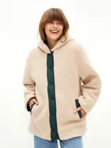 Campera acolchada de color verde oscuro con diseño matelasseado, interior forrado en corderito sintético color beige, con capucha y cierre frontal de botones a presión.