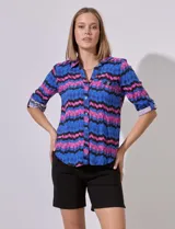 Camisa de manga 3/4 con estampado zig zag en tonos azul, rosa y negro. Tiene cuello con solapa, escote en V, abertura central con botones y bolsillo simulado en el pecho.