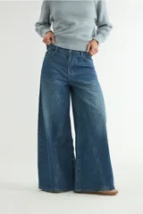 Pantalón de jean azul con corte wide leg y costuras verticales decorativas en el frente. Presenta tiro alto, cierre frontal con botón y bolsillos laterales.