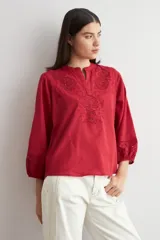 Blusa blanca de corte holgado con cuello mao y escote en V. Presenta detalles de bordado calado en el pecho y en los puños de las mangas tres cuartos.