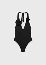 Traje de baño enterizo negro con escote halter y detalle de flor aplicada en el frente. Presenta espalda descubierta y cierre de lazo en el cuello.
