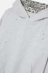 Hoodie cropped de Scuffers en color gris melange, con diseño oversized y detalles distressed. Presenta terminaciones con estampado animal print en la capucha, los puños y la cintura, e incluye un bolsillo frontal tipo canguro.