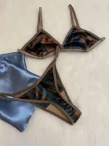 Conjunto de lencería compuesto por un bralette de corte triangular y una tanga regulable. Ambas piezas están confeccionadas en terciopelo con un estampado abstracto en tonos azul, marrón y negro, con terminaciones en ribete color marrón.