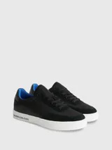 Zapatillas urbanas Calvin Klein con diseño de corte bajo. Presentan una combinación de materiales en la capellada, incluyendo paneles de nailon, cuero y ante en color negro. Destacan por su suela de goma blanca con el logo de la marca estampado en el lateral, forro interior en color azul vibrante y cierre mediante cordones.