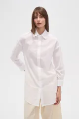 Camisa blanca de algodón con cuello clásico, corte holgado, cierre frontal con botones y mangas largas.
