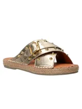 Sandalias tipo ojota con tiras cruzadas en cuero metalizado dorado, decoradas con tachas metálicas y hebilla lateral. Presentan una base con detalle de yute trenzado alrededor del contorno.