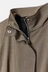 Chaqueta de cuello subido y manga larga con puños elásticos. Presenta un fruncido elástico en la cintura que genera un efecto peplum. Cierre frontal con cremallera oculta por solapa.
