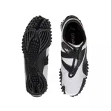 Championes Puma modelo Mostro Perforated, de diseño bajo con exterior de cuero perforado en color blanco y detalles en negro. Presenta una suela distintiva con relieve de tachones y cierre de velcro en el empeine.
