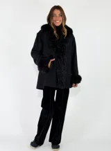 Chaqueta midi color crudo con detalles de piel sintética en el cuello y los puños. Presenta un diseño abierto con bolsillos laterales y una textura suave.