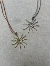 Collar con dije de sol espiral plateado y cordón marrón.