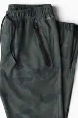 Pantalón de jogging deportivo de corte estándar, color verde militar con estampado de camuflaje pixelado. Confeccionado en tejido funcional DryMove™ con elasticidad en cuatro direcciones. Presenta cintura elástica con cordón de ajuste, bolsillos al bies con cierre y bajos ajustados con cierre y elástico.