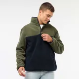 Buzo de polar efecto borreguito con diseño color block en verde oliva y azul marino. Presenta cuello alto con cierre de botones a presión y mangas largas.