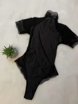 Body de lycra color negro con cuello alto, mangas cortas de microtul y detalles de encaje en el cuello, mangas y laterales. Presenta un diseño entallado con espalda descubierta.