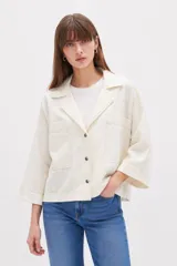 Sobrecamisa de lino y viscosa color marfil, con cuello solapa, mangas tres cuartos anchas, bolsillos frontales con solapa y cierre de botones oscuros.