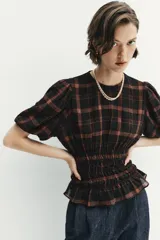 Camisa de cuello redondo y manga corta abullonada, con diseño de cuadros en tonos negro y marrón. Presenta un cuerpo entallado mediante frunces elásticos en la cintura y cierre posterior con abertura y botón.