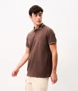 Remera polo masculina de tejido piqué marrón con textura, cuello y ribetes de mangas en tono contrastante, cierre frontal de dos botones y un bolsillo aplicado en el pecho.