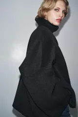 Cazadora de corte amplio confeccionada en hilatura con lana, color beige. Presenta cuello subido, manga larga y cierre frontal con botones negros. Destaca por sus acabados con costuras de hilo a contraste en los bordes.