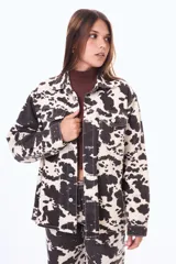 Camisa de denim con estampado animal print tipo vaca en tonos blanco y negro, de corte oversize, con cuello camisero, cierre frontal con botones metálicos y bolsillos con solapa en el pecho.