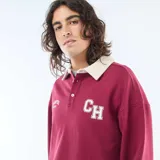 Remera estilo rugby de manga larga en color bordó, con cuello tipo polo en contraste color crema y cierre frontal con botones. Presenta estampado gráfico universitario en el pecho.