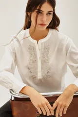 Camisa de algodón color blanco, con cuello redondo, cierre frontal parcial con botones y detalle de bordado con canutillos en el frente.